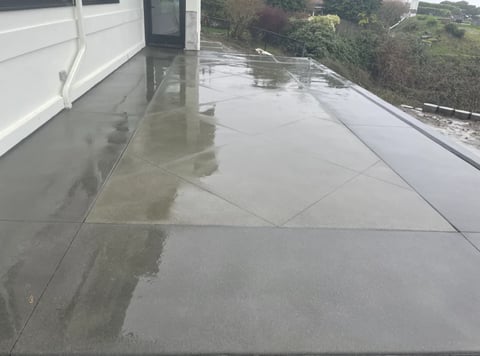 Wet concrete rooftop with pooled water reflecting the sky and surrounding landscape with trees