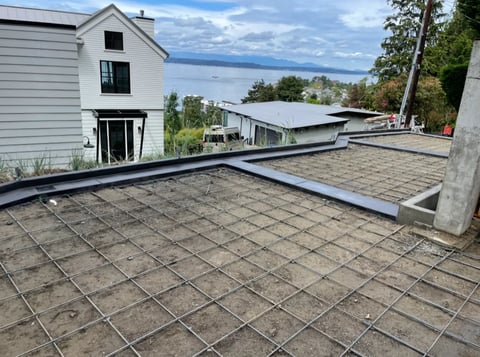 Construction site with wire mesh flooring, white house, and lake view in background