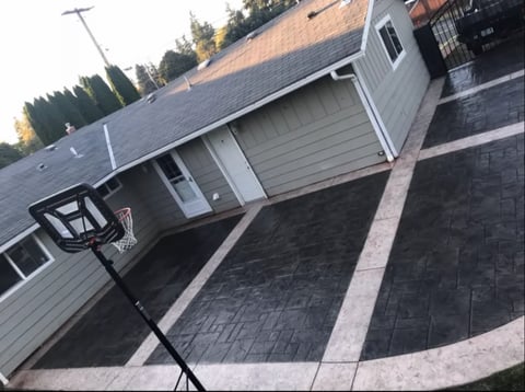Aerial view of a residential driveway with a modern house, black asphalt, and basketball hoop on the side