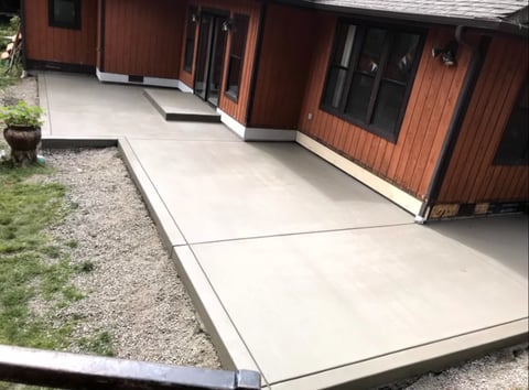 Modern concrete patio extending from a red wooden house with black windows and trim