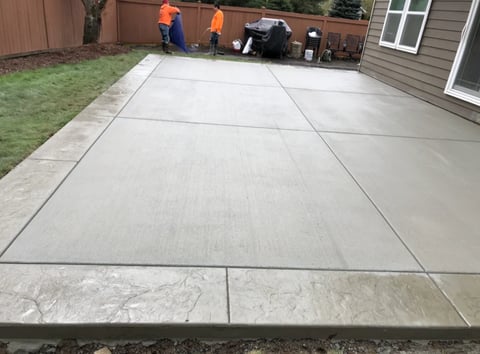 Newly poured concrete patio with control joints in a residential backyard, workers visible in background
