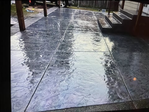 Wet concrete patio or deck with water pooling and reflections, wooden posts and railings visible on sides