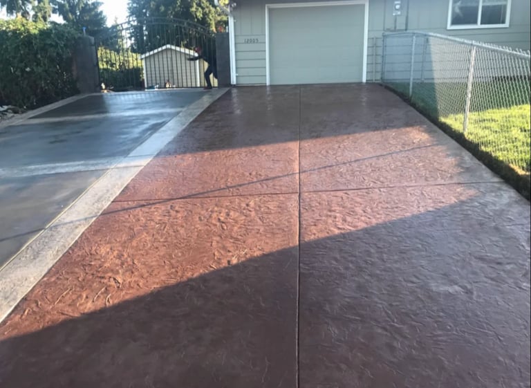Concrete driveway with brown and dark stain pattern, residential home with fence in background
