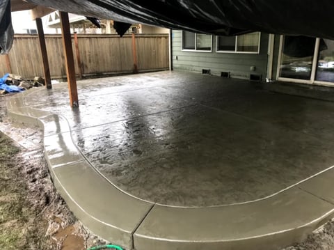 Newly poured concrete patio in backyard with wooden fence and house in background