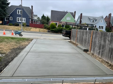 Newly poured concrete driveway with traffic cones alongside residential houses and wooden fence