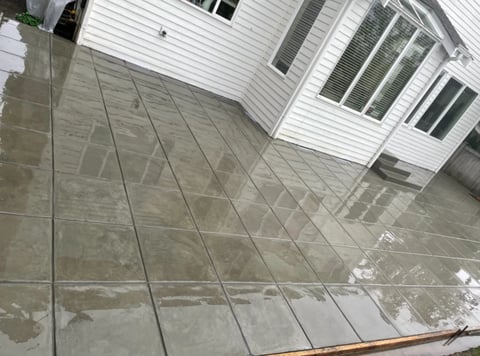 Residential driveway with large grey tiles adjacent to white siding house with windows