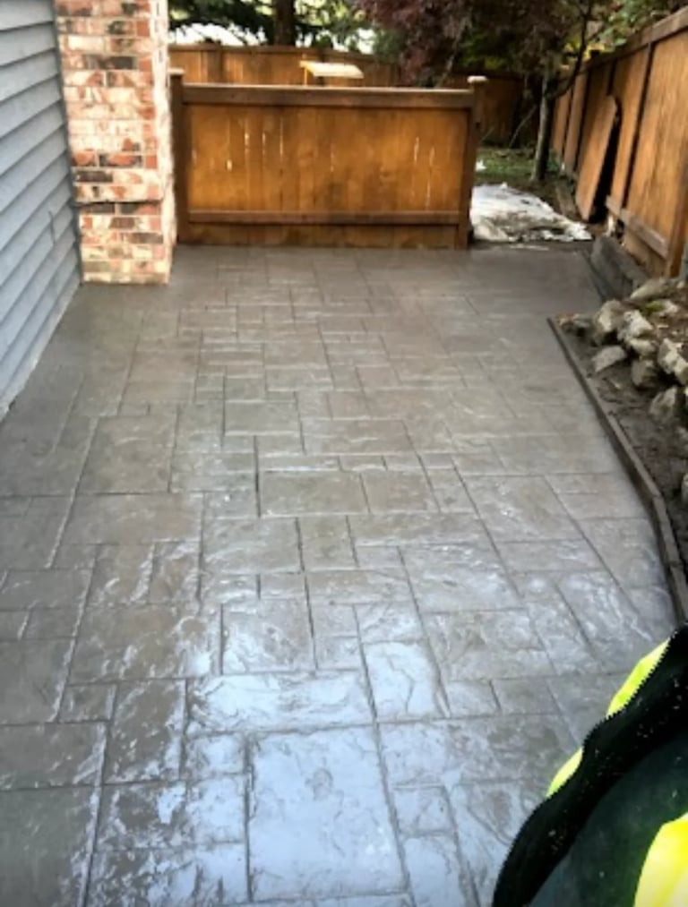 Wet paved driveway with herringbone brick pattern, wooden gate, and house exterior