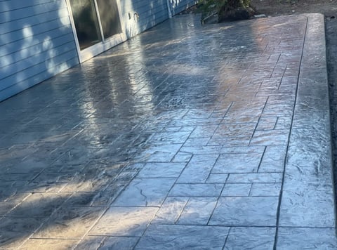 Wet concrete patio with herringbone pattern under afternoon sunlight, near a white building wall